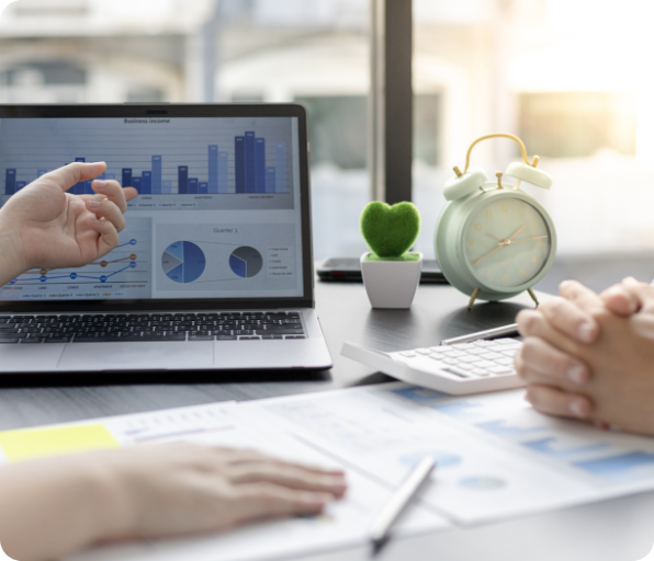A person pointing to a financial chart on a laptop screen while explaining a business report to a colleague.
